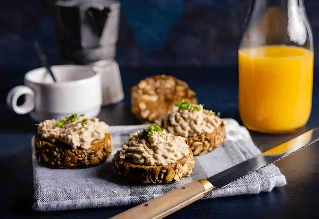  A plate of tuna loaf  on small round bread rolls, with a knife, a cup, and a glass of orange juice in the background